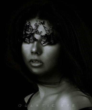 Visage féminin avec des papillons noirs couvrant les yeux sur fond sombre.